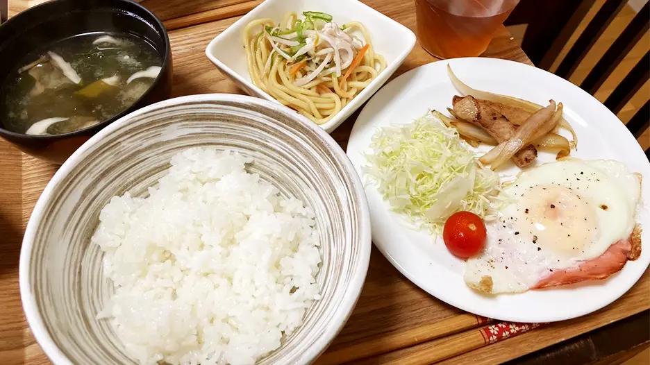 食事の例（ごはん、味噌汁、小鉢、ハムエッグ、千切りキャベツミニトマト他）